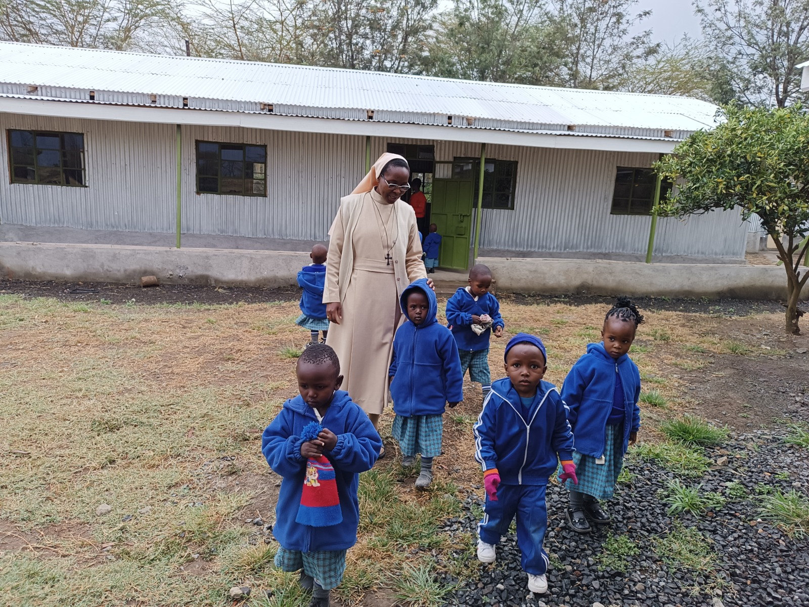 Una hermana camina con niños pequeños frente a la escuela en Kenia